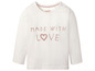 Witte babytrui met lange mouwen van Lupilu met de tekst 'Made with love'.