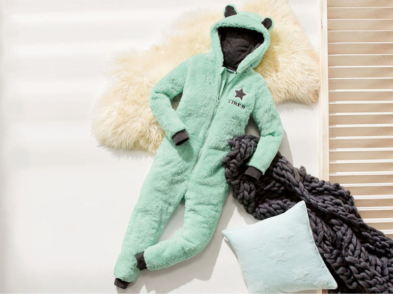 Een groene onesie met capuchon en oren, een grijze deken en een lichtblauwe kussen.