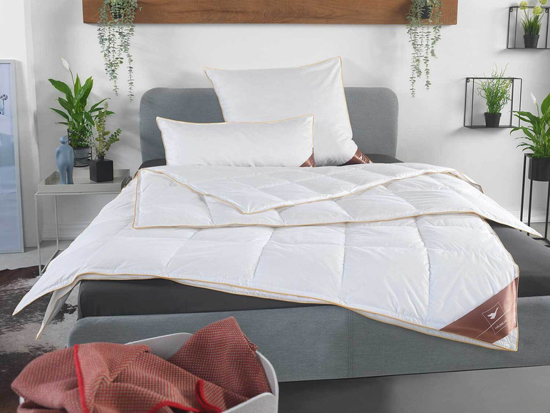 Een wit dekbed met een gouden rand, op een bed met kussens