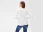 Een vrouw draagt ​​een witte longsleeve en blauwe jeans.