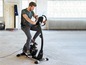 Man fietst op een zwarte hometrainer in een fitnessruimte.
