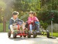 Twee kinderen rijden op een rode en zwarte go-kart met Superman en Batman-thema's.
