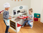 Twee kinderen spelen met een houten speelgoedkeuken met een bestelbord.