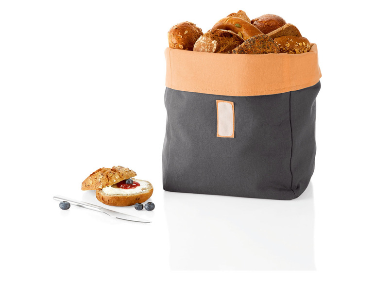 Een grijze broodmand met verschillende soorten brood, inclusief een rol met jam en roomkaas.