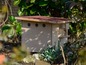 Een houten insectenhotel met een rood dak in een tuin.