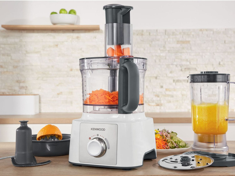 Een Kenwood keukenmachine met gesneden wortels, een blender met sinaasappelsap en verschillende accessoires.