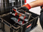 Een hand die een doos met schroeven en moeren in een zwarte Qbrick-kist plaatst.