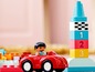 Een rode auto met een LEGO Duplo figuurtje, naast een toren met nummerblokken.