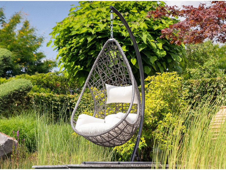 Een grijze hangstoel met witte kussens in een tuin.