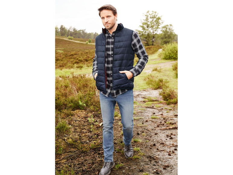 Man in een blauwe gewatteerde vest, geruit overhemd en jeans.