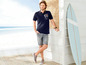 Man in blauwe polo en korte broek met surfplank.