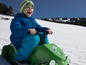 Een kind rijdt op een groene sneeuwscooter in de sneeuw.
