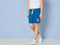 Een kind draagt blauwe shorts met een Paw Patrol-print en witte sneakers.