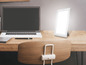 Een laptop en een lichttherapie lamp op een houten bureau.