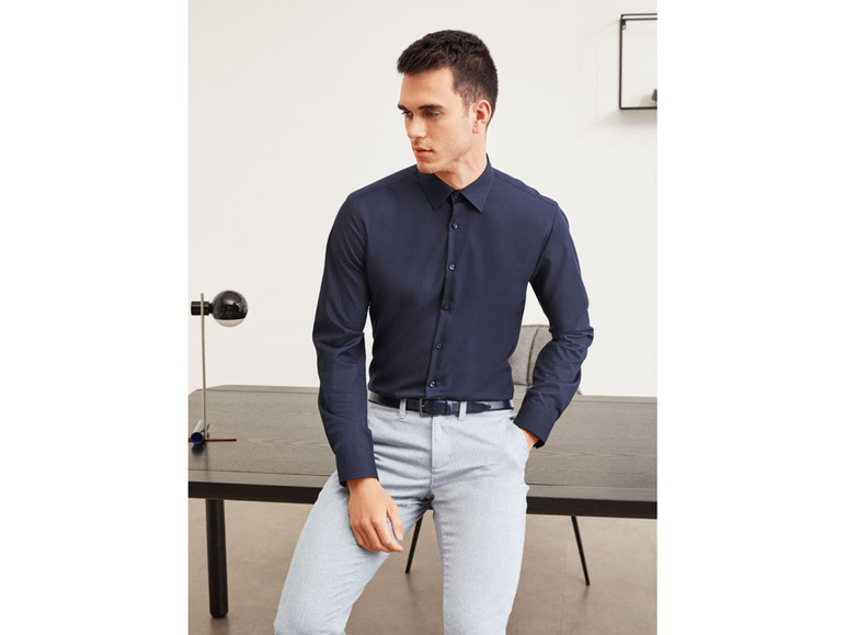 Een man draagt een donkerblauw overhemd en grijze broek.