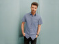 Man in een geblokt overhemd poseert voor een blauwe muur.