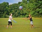 Twee mensen spelen met een blauwe bal en foam-stokken op gras.