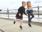 Twee kinderen spelen hopscotch met een blauwe jurk en een gestreepte trui.
