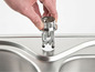 Een hand plaatst een kraan op een RVS spoelbak.