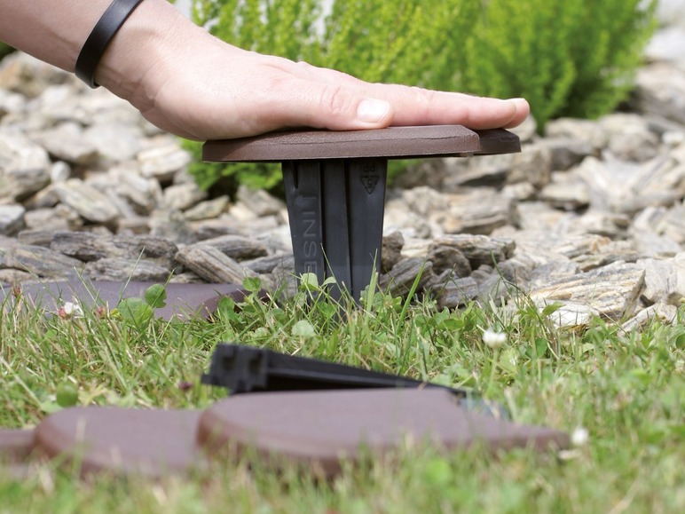 Een hand die op een bruine INSE tuinrand drukt.