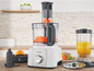 Een Kenwood keukenmachine met gesneden wortels, een blender met sinaasappelsap en verschillende accessoires.