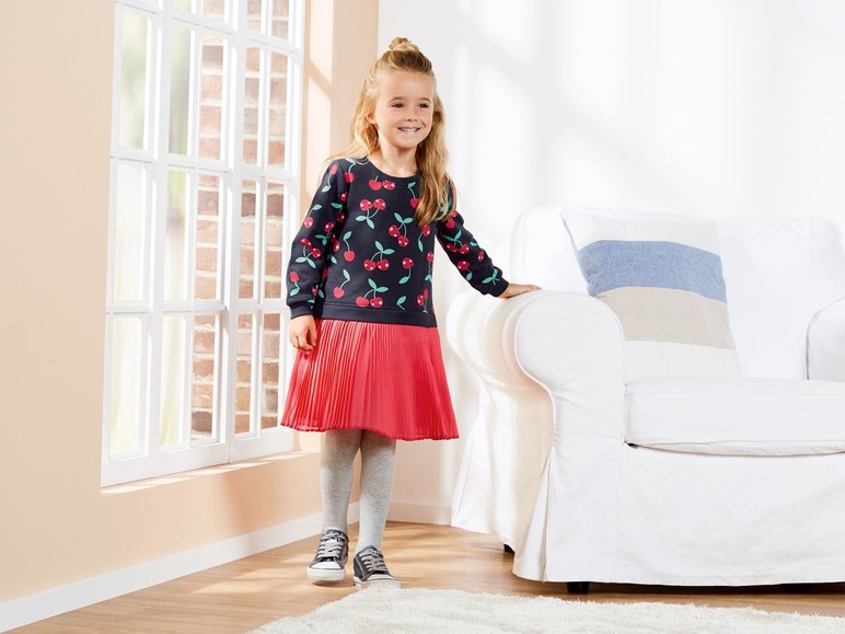 Een meisje draagt een donkerblauwe trui met kersenprint en een roze rok.