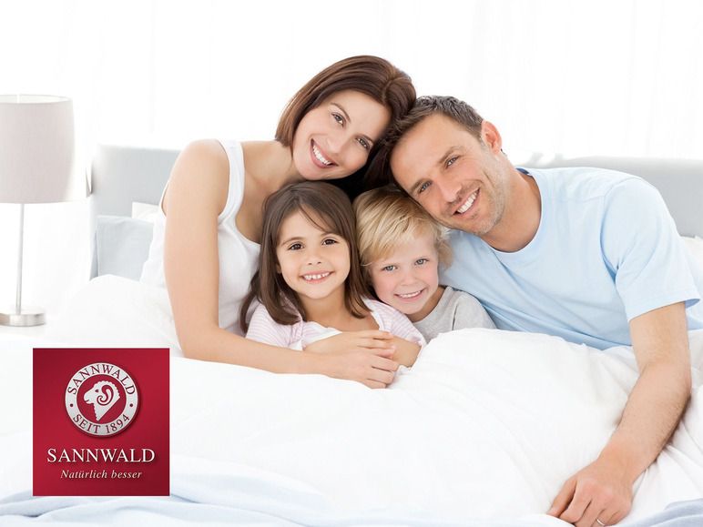 Een gezin glimlacht in bed met Sannwald beddengoed.