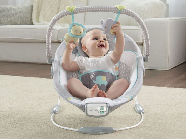 Een baby zit in een grijze Ingenuity baby-schommelstoel met een leeuw en olifant speelgoed.