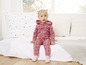 Een meisje in een roze jumpsuit met Mickey Mouse print, zittend op een bed.