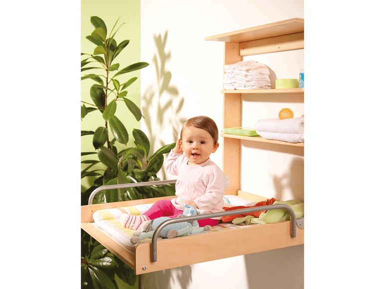 Een baby op een verschoningskussen met een houten wandrek met luiers en badproducten.