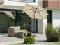 Een beige parasol met een wicker loungeset op een terras.