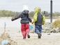 Twee kinderen in regenkleding lopen op het strand.