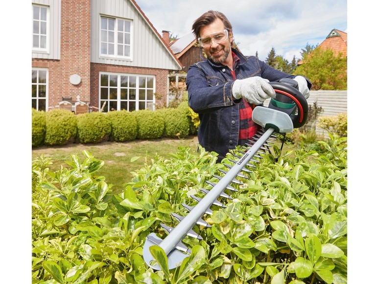 Een man trimmet een haag met een elektrische heggenschaar van Gardena.