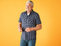Een man in een geruit overhemd en zonnebril staat voor een gele achtergrond.