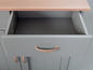 Een open lade van een grijs dressoir met koperen handvatten.