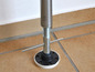 Een metalen paal met een schroefdraad en een zwarte voet op een tegelvloer.