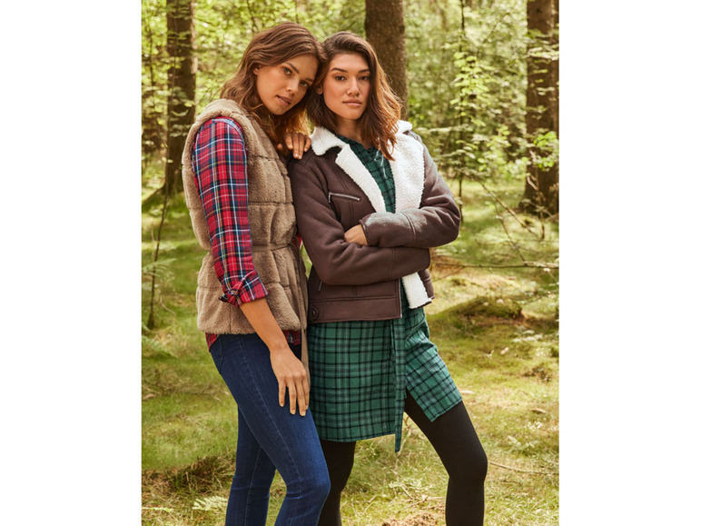 Twee vrouwen in een bos, één draagt een bruin vest en de andere een donkerbruine jas.