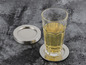 Een glas met een drankje op een zilveren onderzetter met een stapel zilveren onderzetters ernaast.