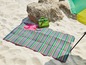 Een gestreept strandkleed op het strand met een groene tas en zonnebrillen.