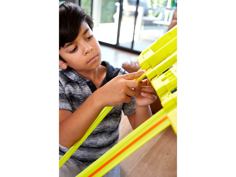 Een kind bouwt een Hot Wheels-baan met gele onderdelen.
