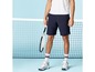 Man met tennisracket en blauwe shorts voor de tennisbaan.