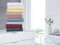 Stapel beddengoed in verschillende kleuren op een witte commode.