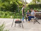 Een groep mensen geniet van een barbecue in de tuin met een driepoot en een barbecue.