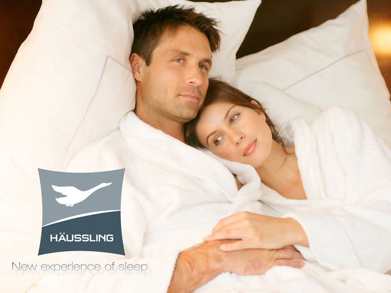 Een stel in witte badjassen ligt in bed met Häussling beddengoed.