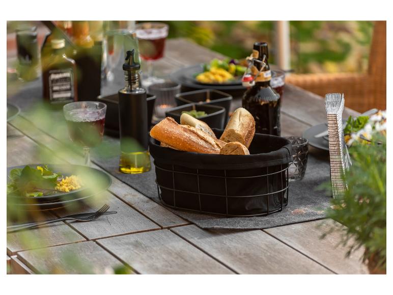 Een zwarte broodmand met stokbrood op een houten tafel tijdens een buiten diner.