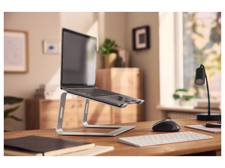 Laptop op een standaard, muis en toetsenbord op een houten bureau in een thuiskantoor.