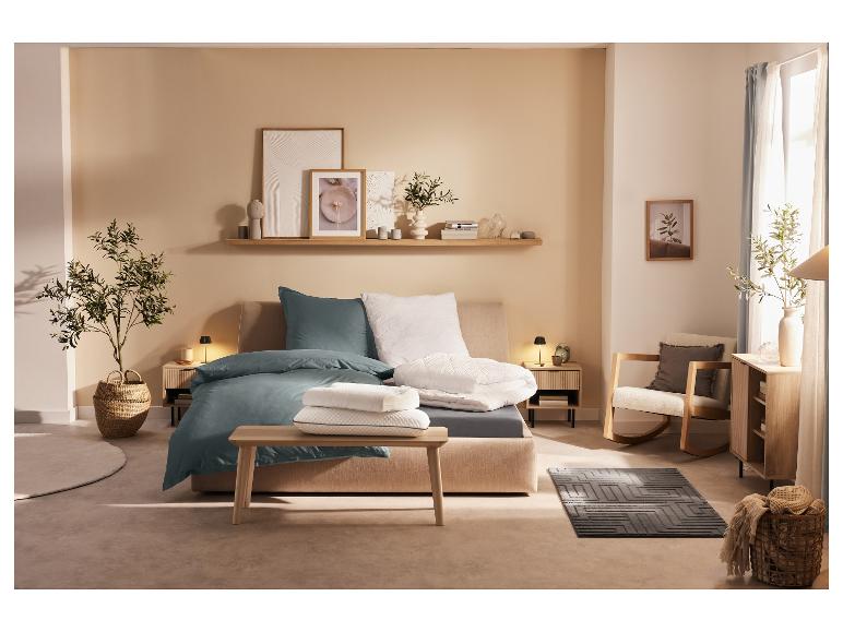 Bed met blauwgroen beddengoed en minimalistische slaapkameraccessoires.