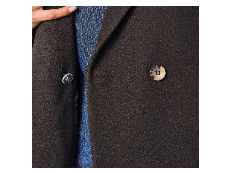 Close-up van een donkerbruine blazer met twee knopen, gedragen over een blauw spijkeroverhemd.