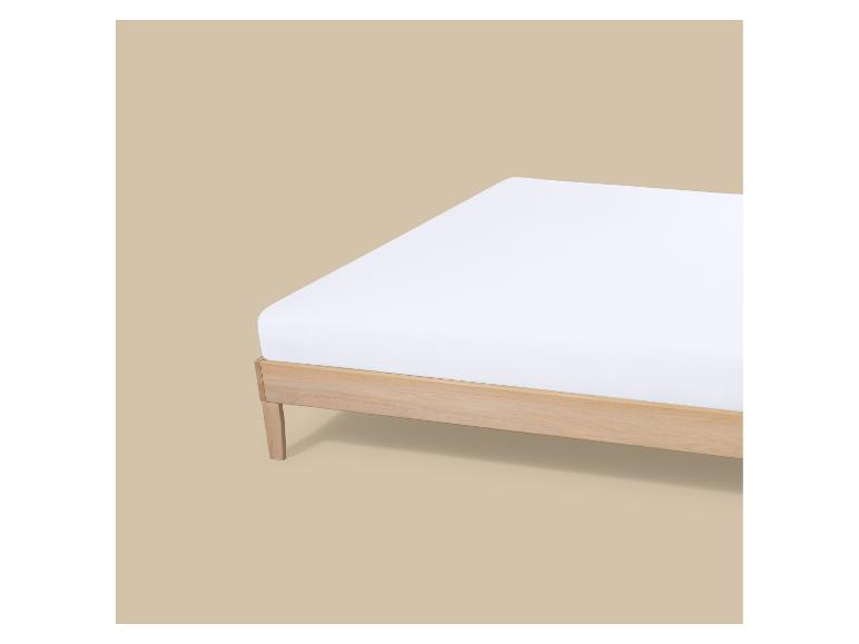 Wit matras op een licht houten bedframe tegen een beige achtergrond.