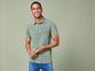 Man in een groene polo en blauwe jeans.